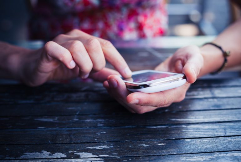 A young woman is using her smart phone at a table outside