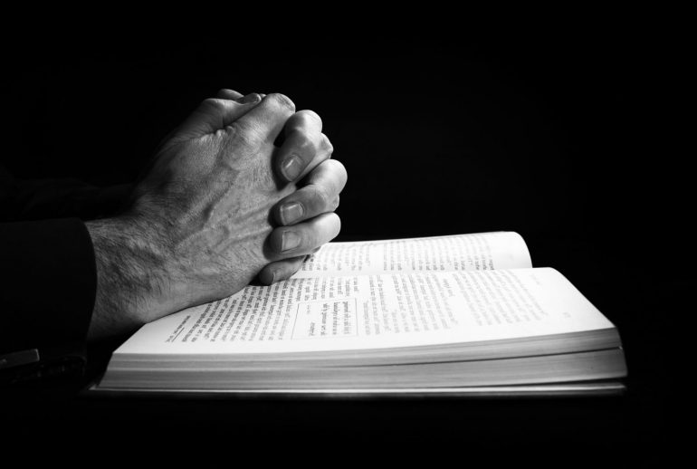 Man praying on the holy bible. The image has intentional added grain and styling.