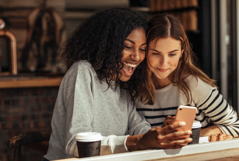 Two,Women,Sitting,In,A,Restaurant,Looking,At,Mobile,Phone