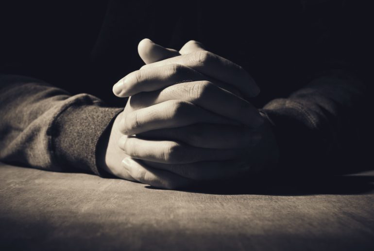 Praying,Hands,Of,Young,Man,On,A,Wooden,Desk,Background.